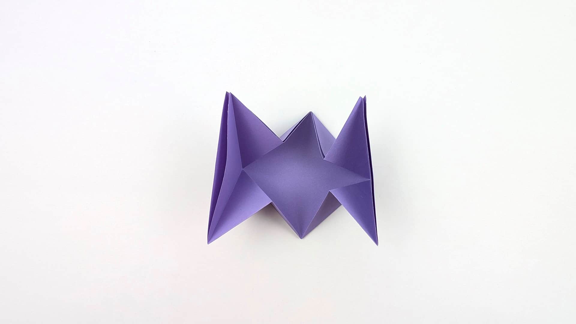 Push in at both sides along the existing creases to collapse into a 3D shape. Four raised points appear — like a bat wing or accordion.