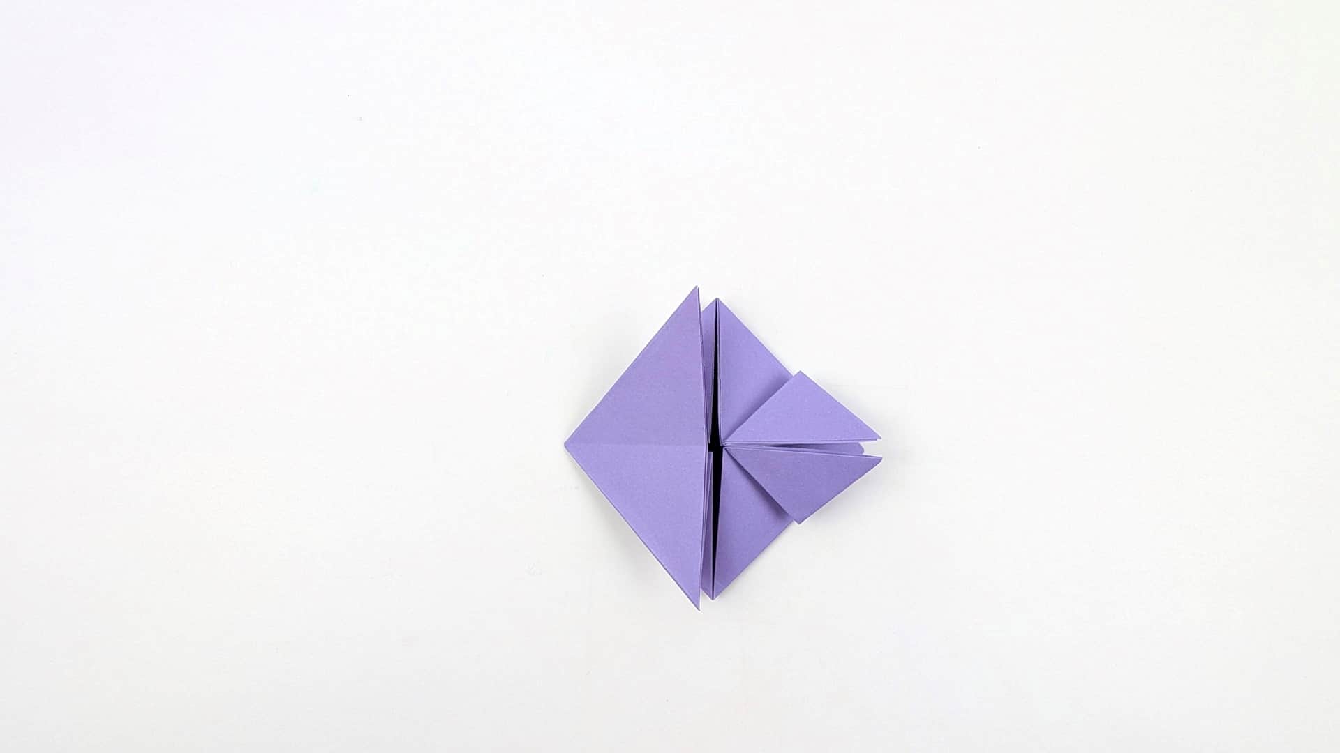 Continue folding the right flap inward. Multiple layers compress toward the center, making the shape more compact.