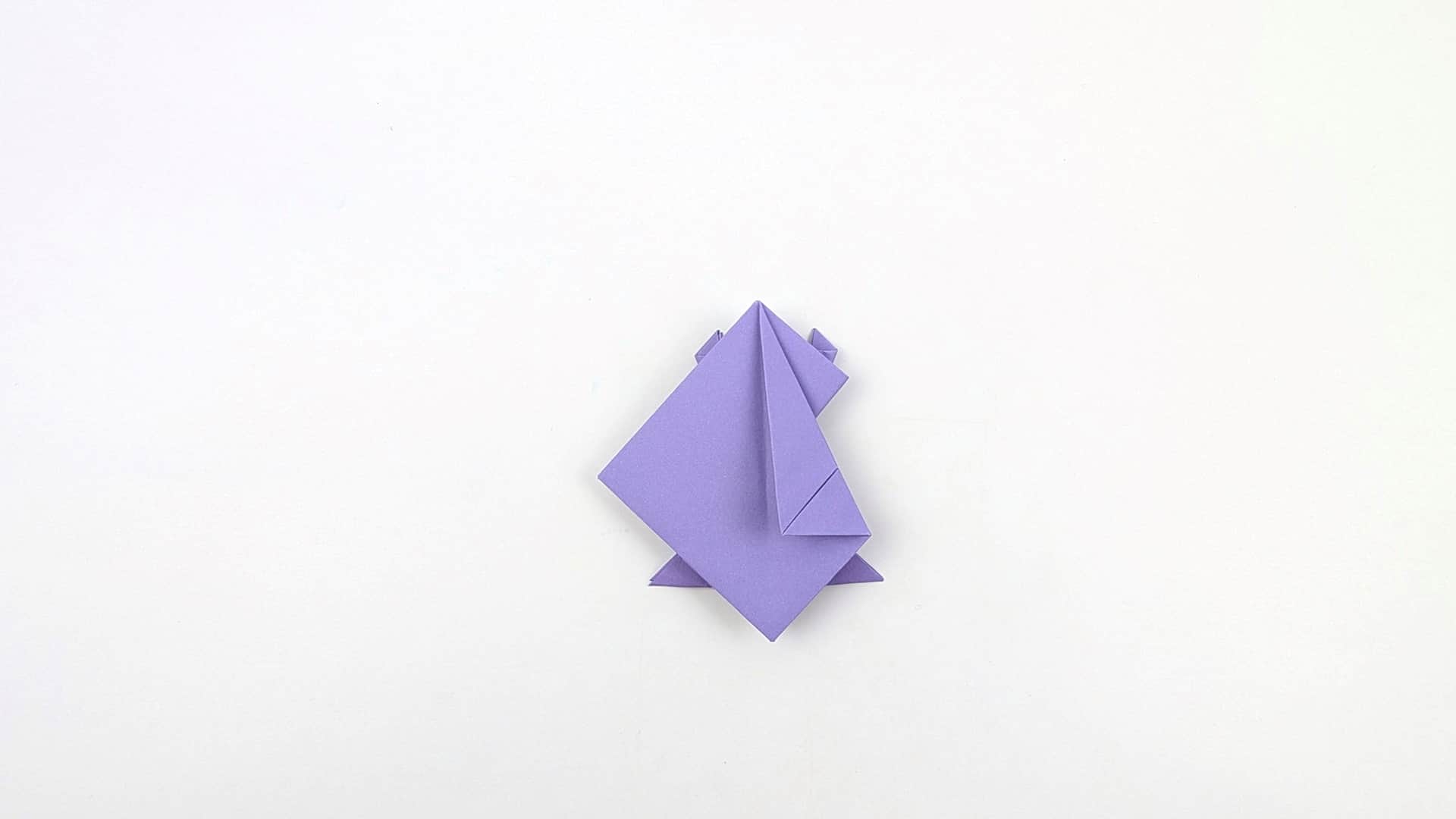 Fold the top half of the model down over the bottom half. The frog's body and head shape begins to emerge, with front and back legs visible.